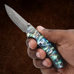 Hand holding a pocket knife with abalone handle and etched blade