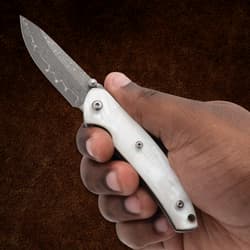Hand holding a white-handled knife with a patterned blade