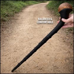 Hand holding a black walking cane with a wooden handle on a dirt path
