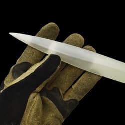 Shining silver double edged narrow blade being held at its' end by a glove covered hand.