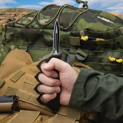 Person holding tactical knife with camo backpack in background