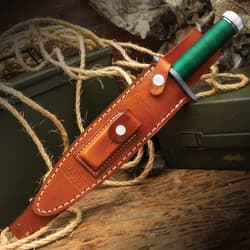 The Rambo I Signature Edition Knife is secured in a brown leather sheath. The sheath features detailed stitching, a snap closure, and an embossed “Rambo First Blood” logo.