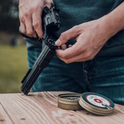 Person loading black air pistol with pellets on wooden table