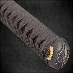 A close view of a black katana scabbard with a black and gold knob wrapped with a black cord