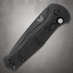 Closed black folding knife with textured grip on gray surface