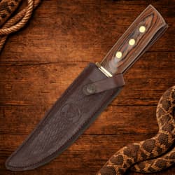 Knife in leather sheath on wooden background with rope