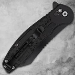 Closed black folding knife with pocket clip on gray background