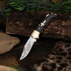 Knife with cross inlay on wooden surface with foliage