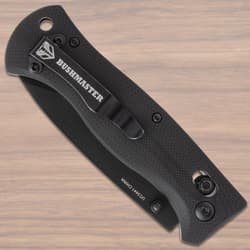 Closed black folding knife with Bushmaster clip on wood surface