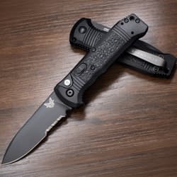 Two black folding knives, one open, on a wooden surface