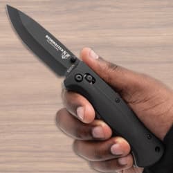 Hand holding open black folding knife on wood background