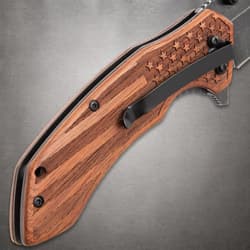 Close-up of the engraved wooden handle with a pocket clip on the GET THE EDGE knife, featuring an American flag design