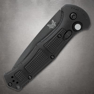 Closed black folding knife with textured grip on gray surface