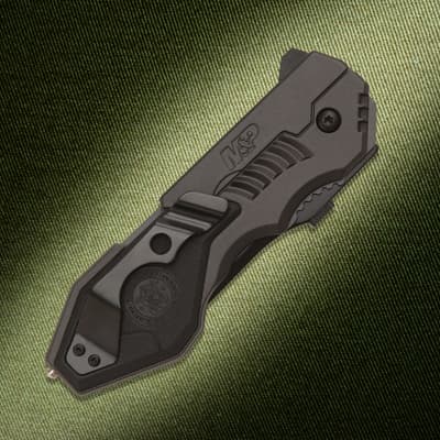Closed black tactical knife with clip on textured background