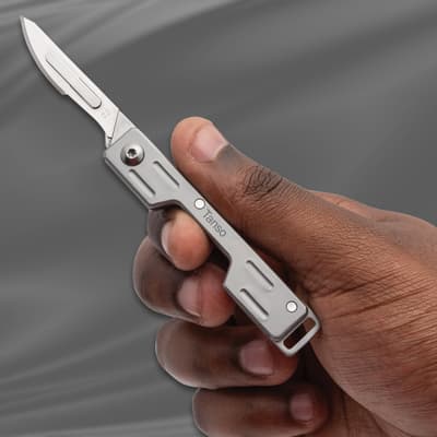 Hand holding a Tanso scalpel knife against a gray background