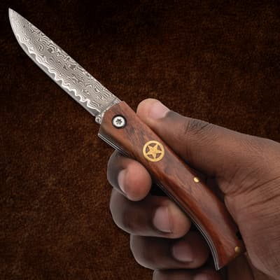 Hand holding a folding knife with a patterned blade