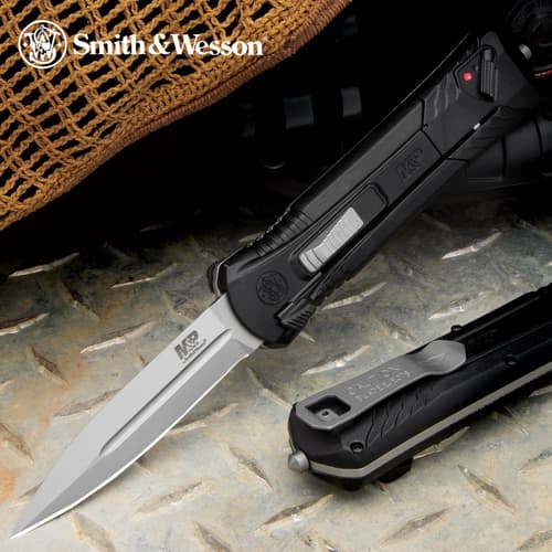 OTF pocket knife with a satin black handle and matte steel blade and sliding trigger button on a metal background.