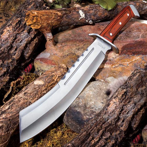 Fixed blade machete with mirror polished blade and wooden handle on a background of wood and rock.