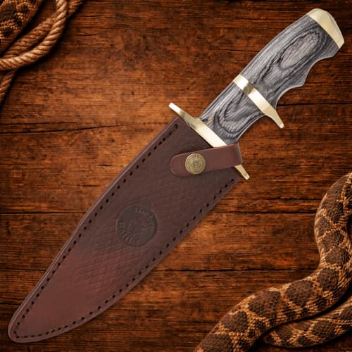 Knife partially sheathed in brown leather on wood background