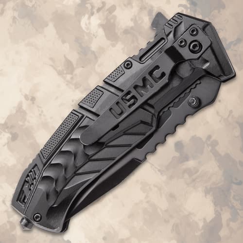Closed black tactical knife with USMC logo on textured background