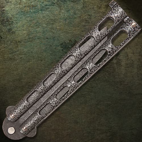 The butterfly knife’s blade is secured between two dark epoxy coated cast metal handles.