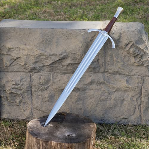 Sword with brown handle leaning against stone and wood outdoors