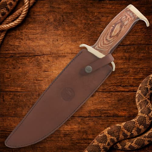 Bowie knife in leather sheath on wooden background
