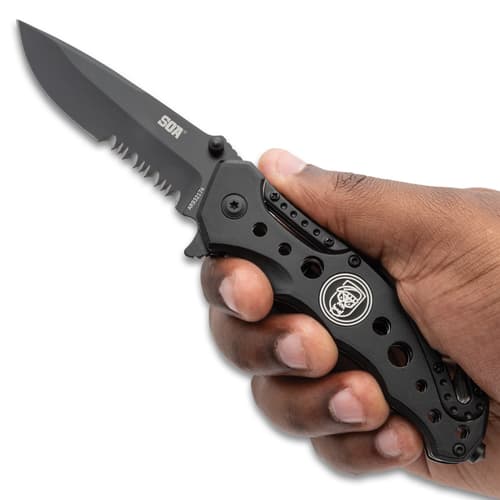 Hand holding a black folding knife with serrated blade