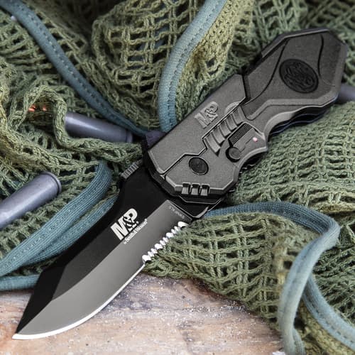 Open tactical knife on green netting with bullets nearby