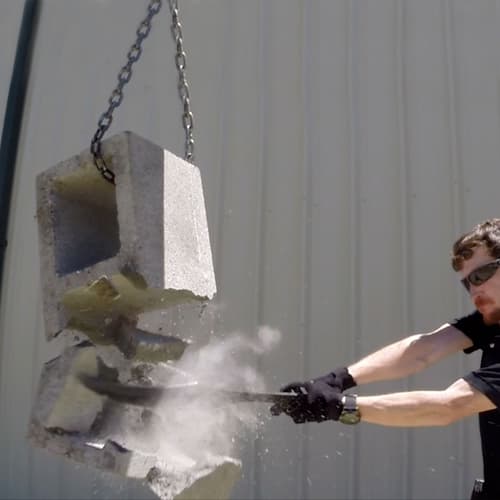 A man uses the 300 Spartan Warrior Replica against a cinder block hanging from a chain.