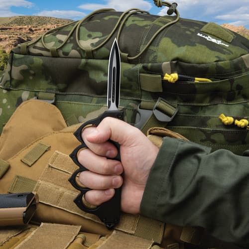 Person holding tactical knife with camo backpack in background