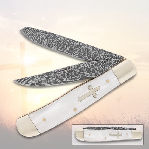Folding knife with patterned blades and cross design on handle, set against a soft background