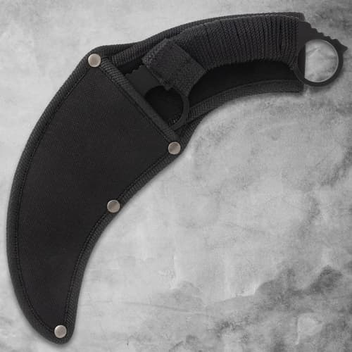 Karambit knife in a black nylon sheath on gray surface
