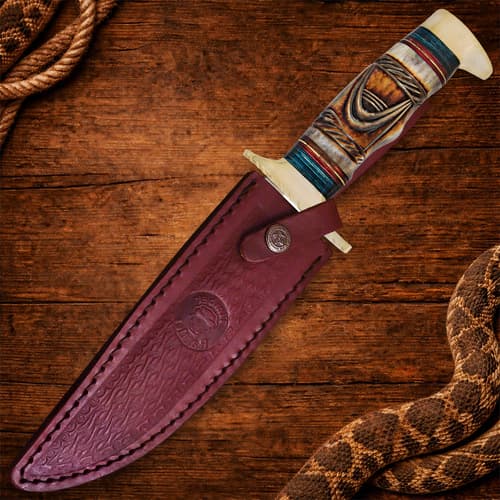 Bowie knife in leather sheath on wooden surface with rope