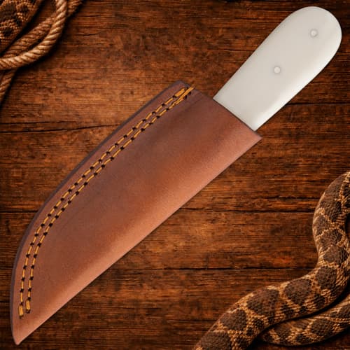 Knife in brown leather sheath on wood background
