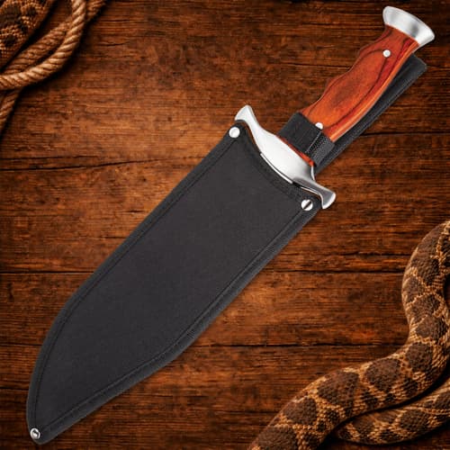 Knife in black sheath with wooden handle on wooden background
