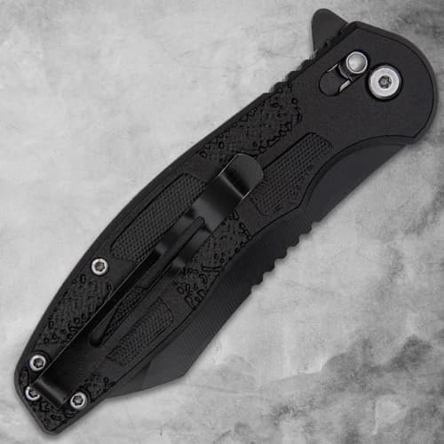 Closed black folding knife with pocket clip on gray background