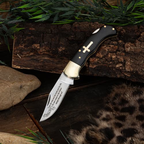 Knife with cross inlay on wooden surface with foliage