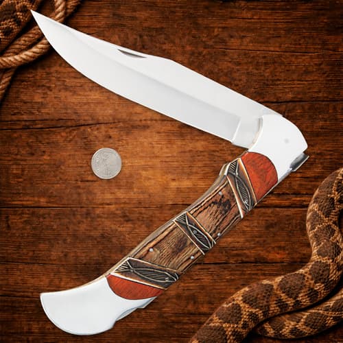 Open folding knife with coin for scale on wooden background