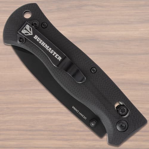 Closed black folding knife with Bushmaster clip on wood surface