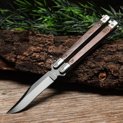 Butterfly knife with wooden handles on a log with greenery