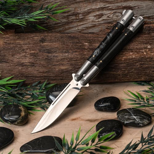 Butterfly knife on wooden surface with stones and leaves