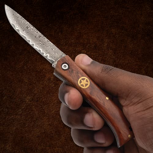 Hand holding a folding knife with a patterned blade