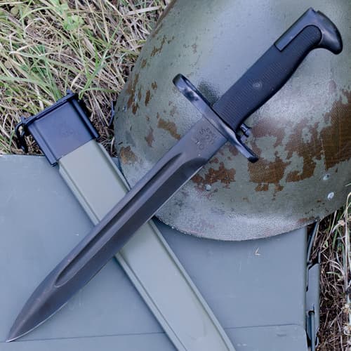 Bayonet and scabbard on grass with a helmet