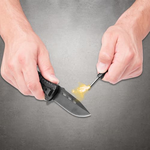 Hands holding an open Black Legion pocket knife and flint rod, with bright sparks beside the blade
