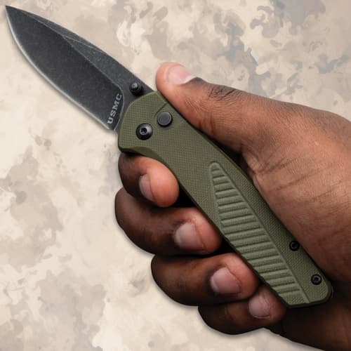 Hand holding a USMC folding knife with green handle