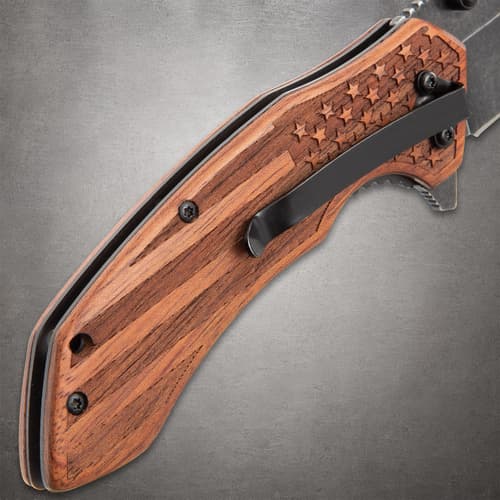 Close-up of the engraved wooden handle with a pocket clip on the GET THE EDGE knife, featuring an American flag design