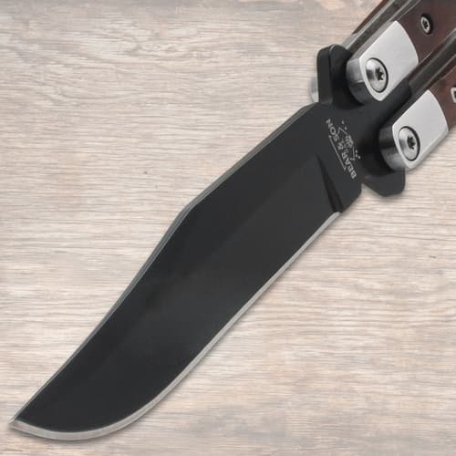 Close-up of butterfly knife's black blade on wood background