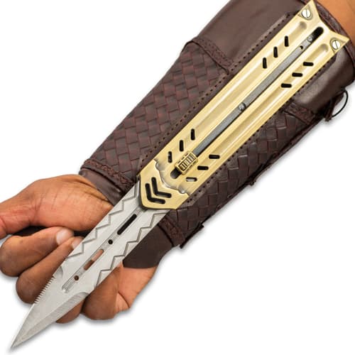 Silver blade with chevron engraving extended over palm of the hand while attached to gold sliding enclosure and mahogany braided faux leather arm sheath.