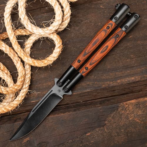 Butterfly knife with wood handle on wooden surface with rope